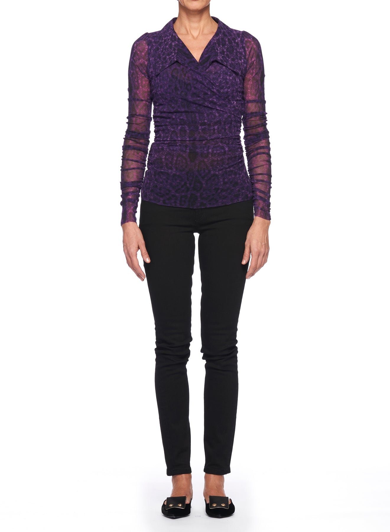 A person stands against a plain white background wearing a vintage piece from Fuzzi—a long-sleeved Fuzzi Woman Purple Mesh Top with a V-neck and patterned design—paired with black fitted pants and black flat shoes. The individual stands with arms relaxed by their sides.