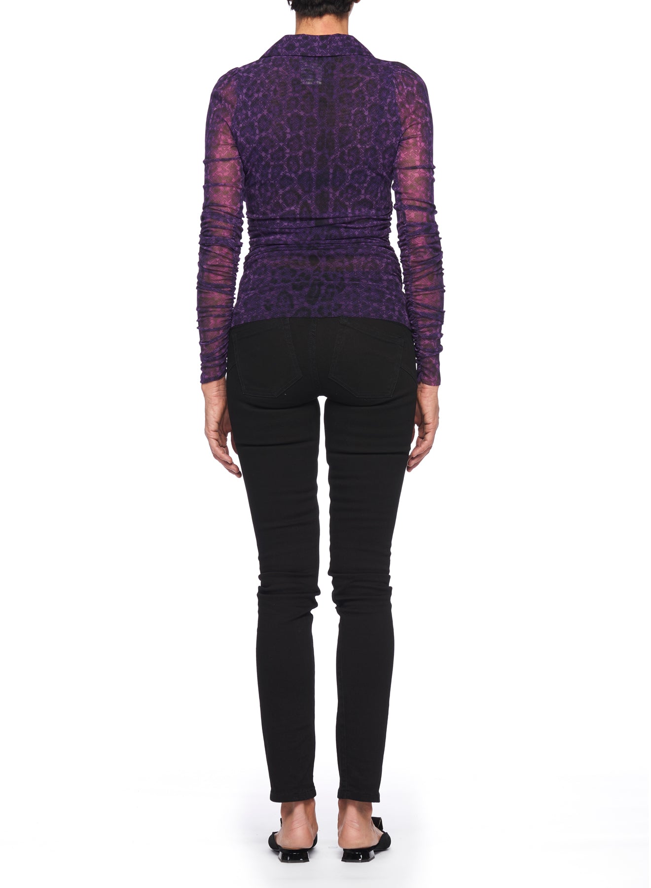 A person stands with their back to the camera, wearing the Fuzzi Woman Purple Mesh Top with V-Neck, featuring a long-sleeve design in a shimmering leopard-print that evokes a vintage feel. Paired with black pants and shoes, they stand against a pristine white background.