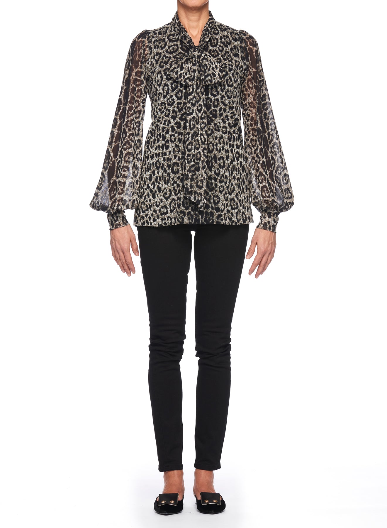 A person stands against a white background wearing the Fuzzi Woman Edgy Mesh Top from Fuzzi, featuring a sheer leopard-print design with puffed sleeves, paired with black pants. The bohemian flair of the mesh top complements their black flat shoes, as their arms rest relaxed at their sides.