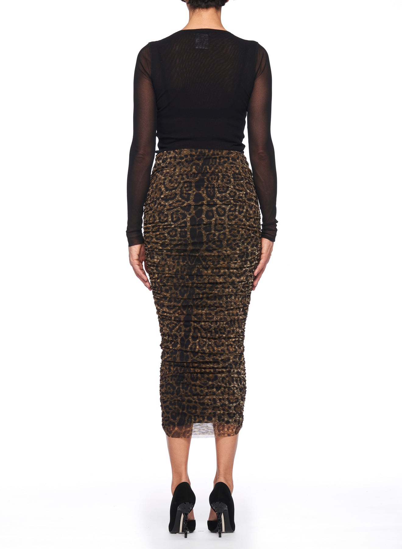 A person stands facing away, wearing the Fuzzi Woman Leopard Print Mesh Skirt featuring a high-waisted design, paired with a long-sleeve black mesh top. They complete the look with sleek black high heels against a plain white background.