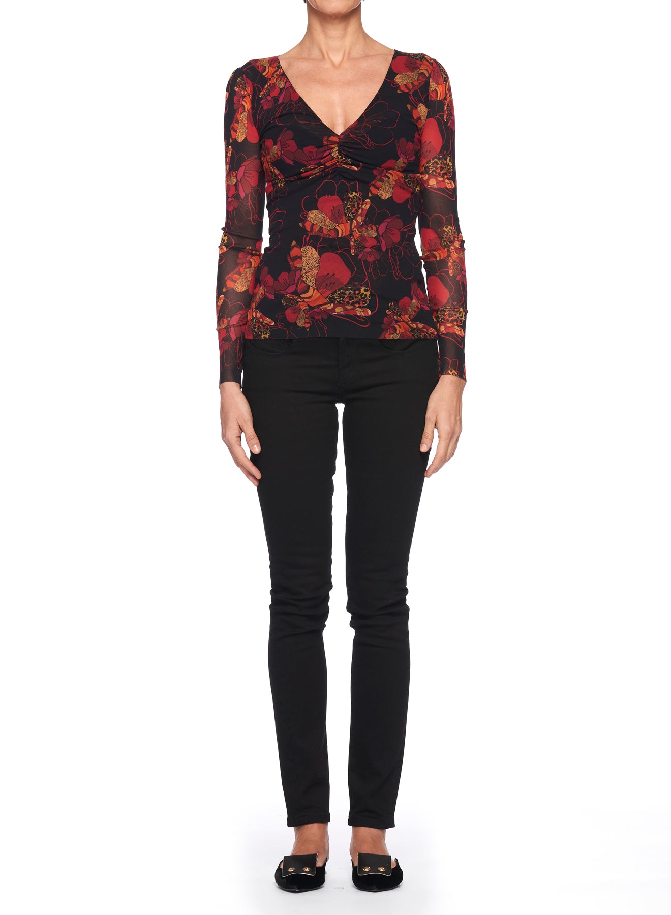 A person is standing against a white background, dressed in the Fuzzi Woman Mesh Top by Fuzzi, which features sheer fabric with red and orange floral designs. They pair it with black pants and black shoes.