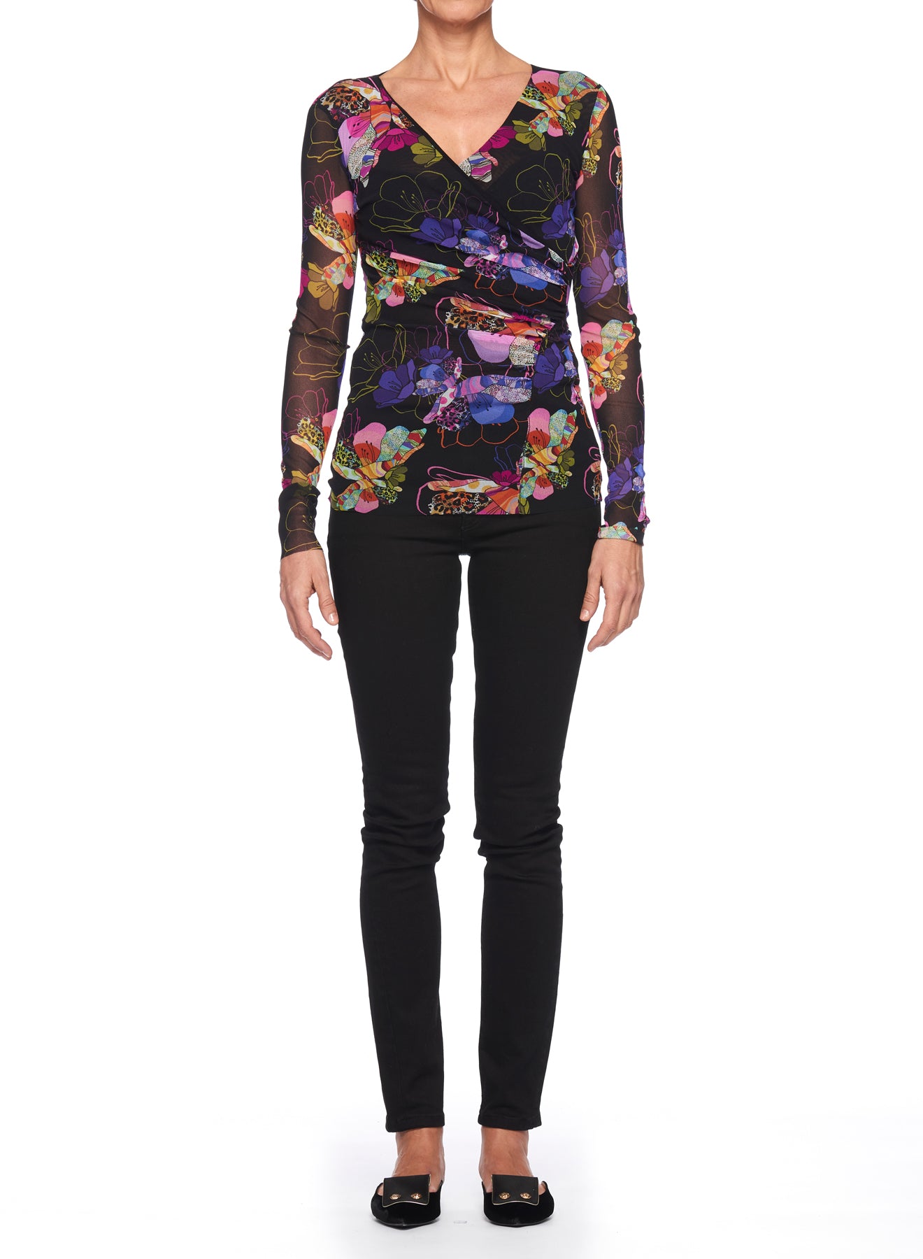 A person wearing the Fuzzi Woman Boho-Chic Floral Mesh Top, featuring a vibrant floral print, and black pants with flat shoes stands against a white background.