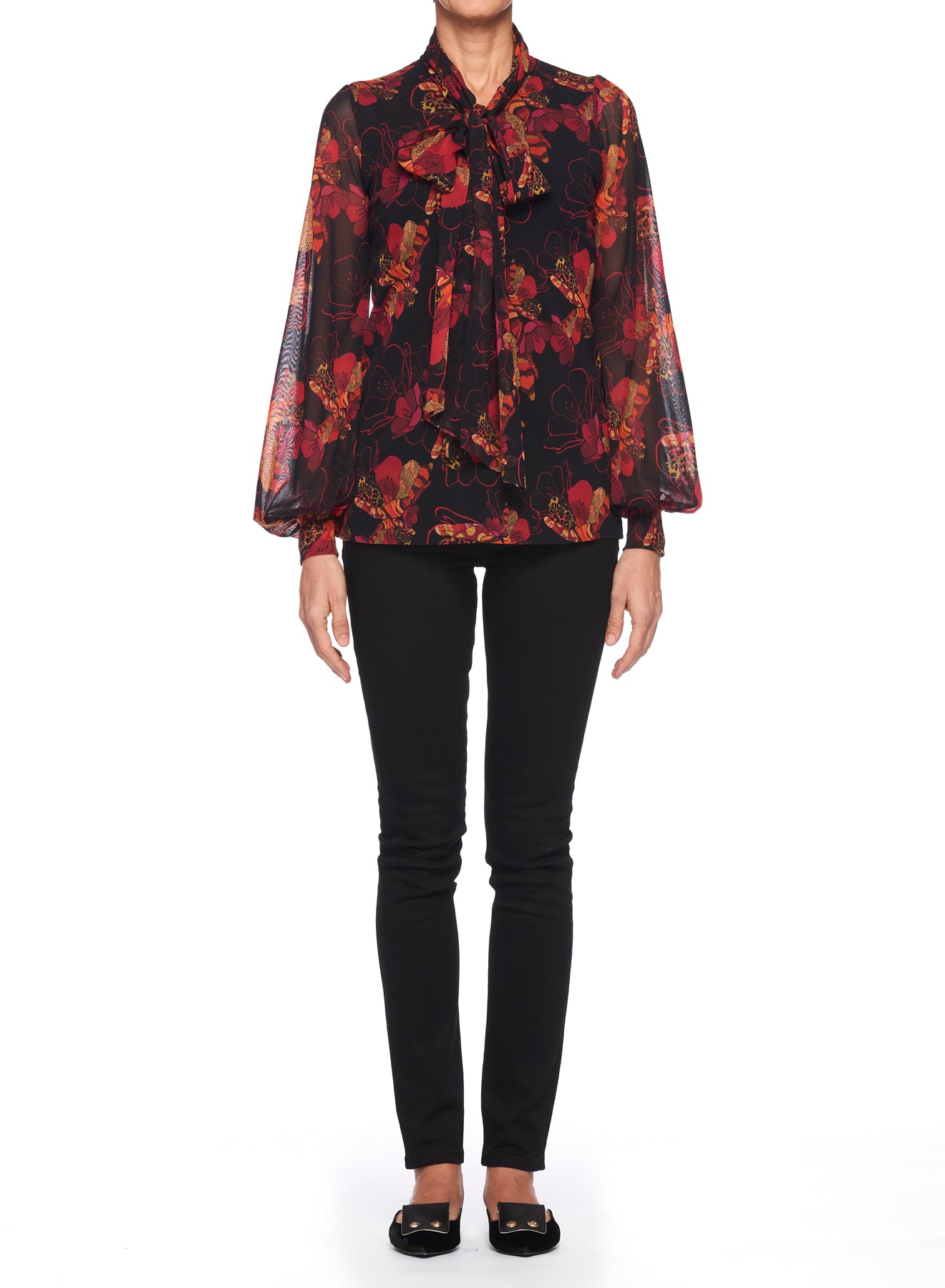 A person is wearing a Fuzzi Woman Romantic Floral Print Blouse with a tie neck, complemented by black fitted pants and black flats. This lovely Fuzzi piece stands out with its sheer fabric featuring a vibrant red and orange floral print. They are standing against a white background.