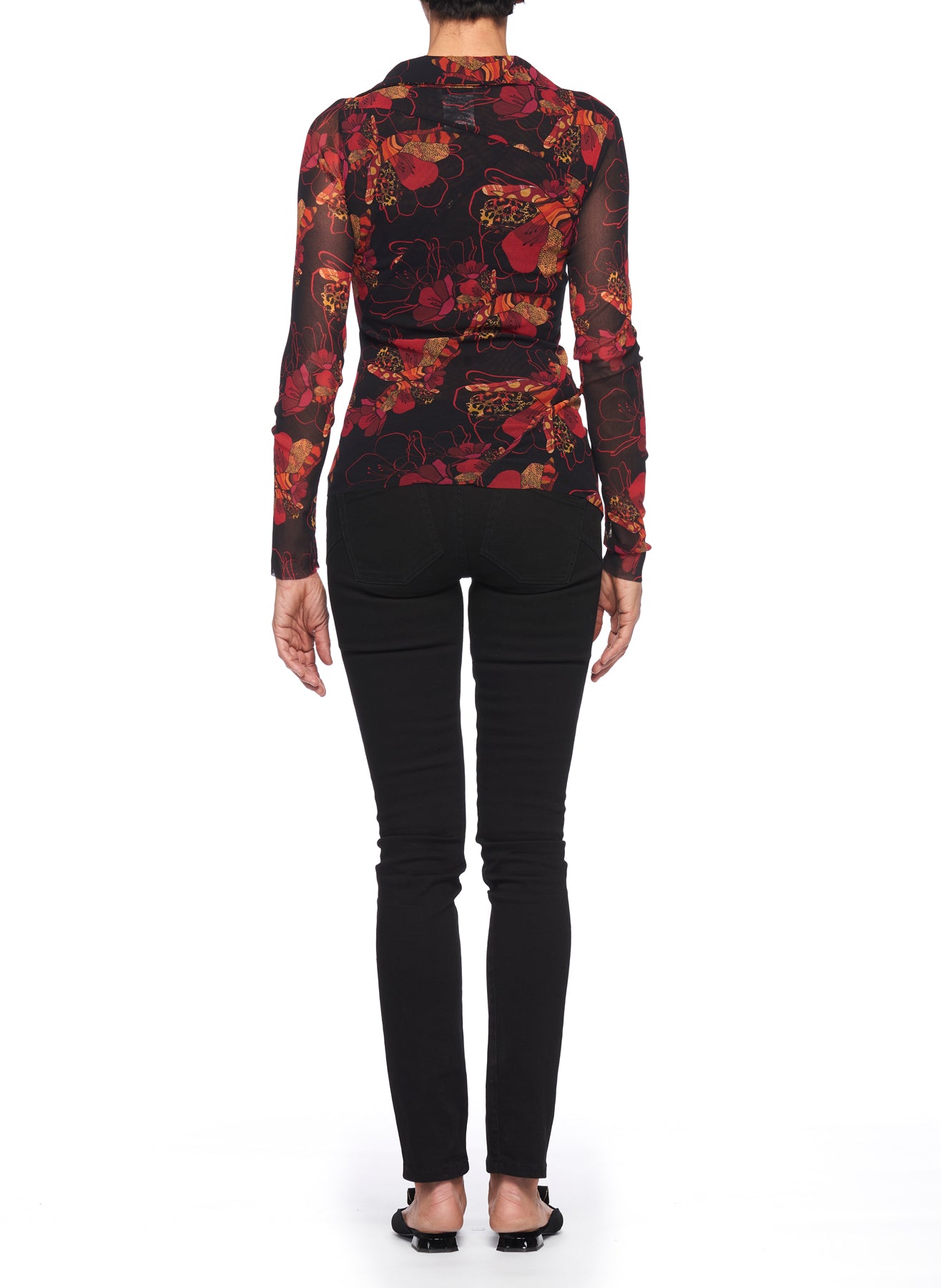 A person stands with their back to the camera, wearing the Fuzzi Woman V-neckline Top, which features a long-sleeved, floral pattern in dark shades evocative of a vintage style. They pair it with black pants and black sandals against a plain white background.