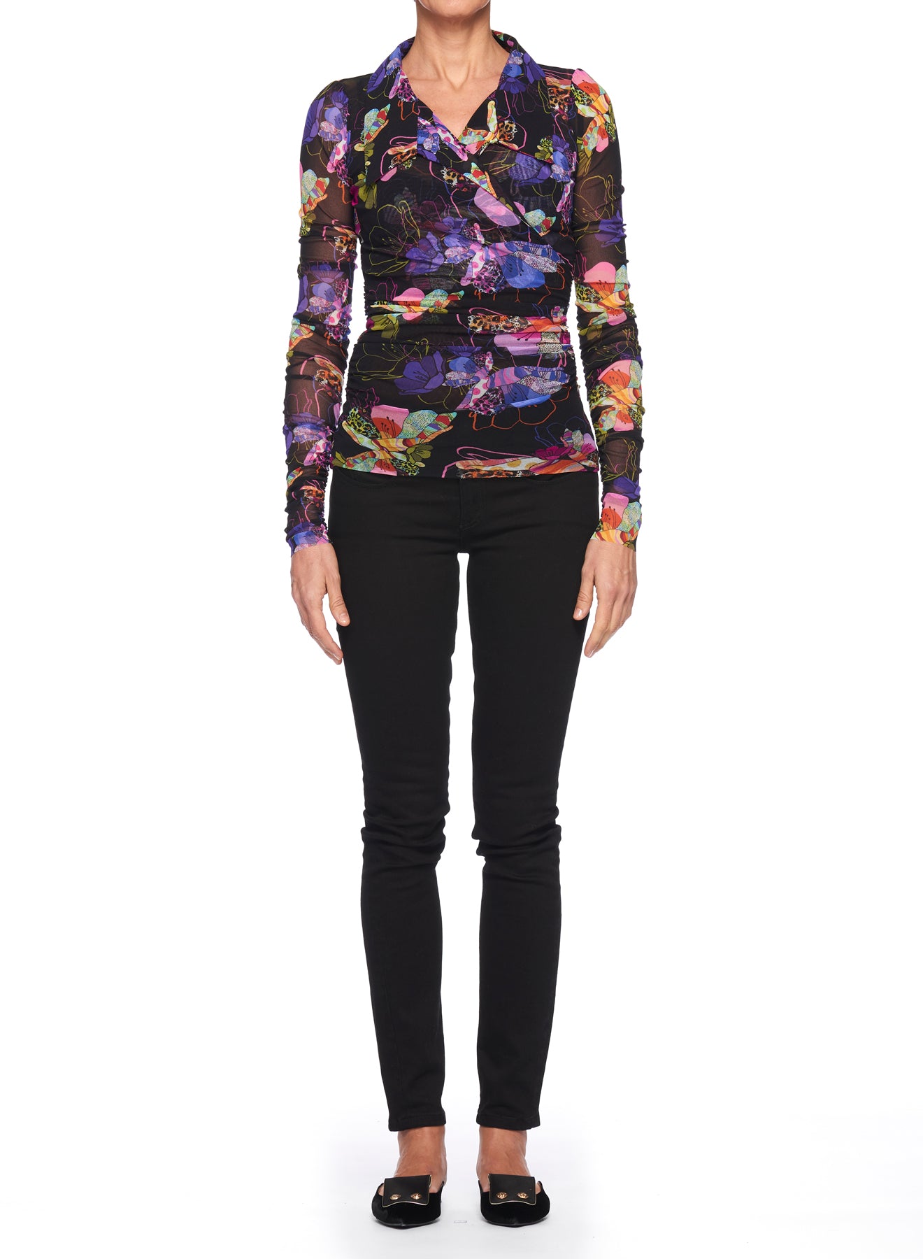 A person stands against a white background, wearing the Fuzzi Woman Boho-Chic Mesh Top with its vibrant bohemian-inspired floral design, paired with black pants and black shoes.