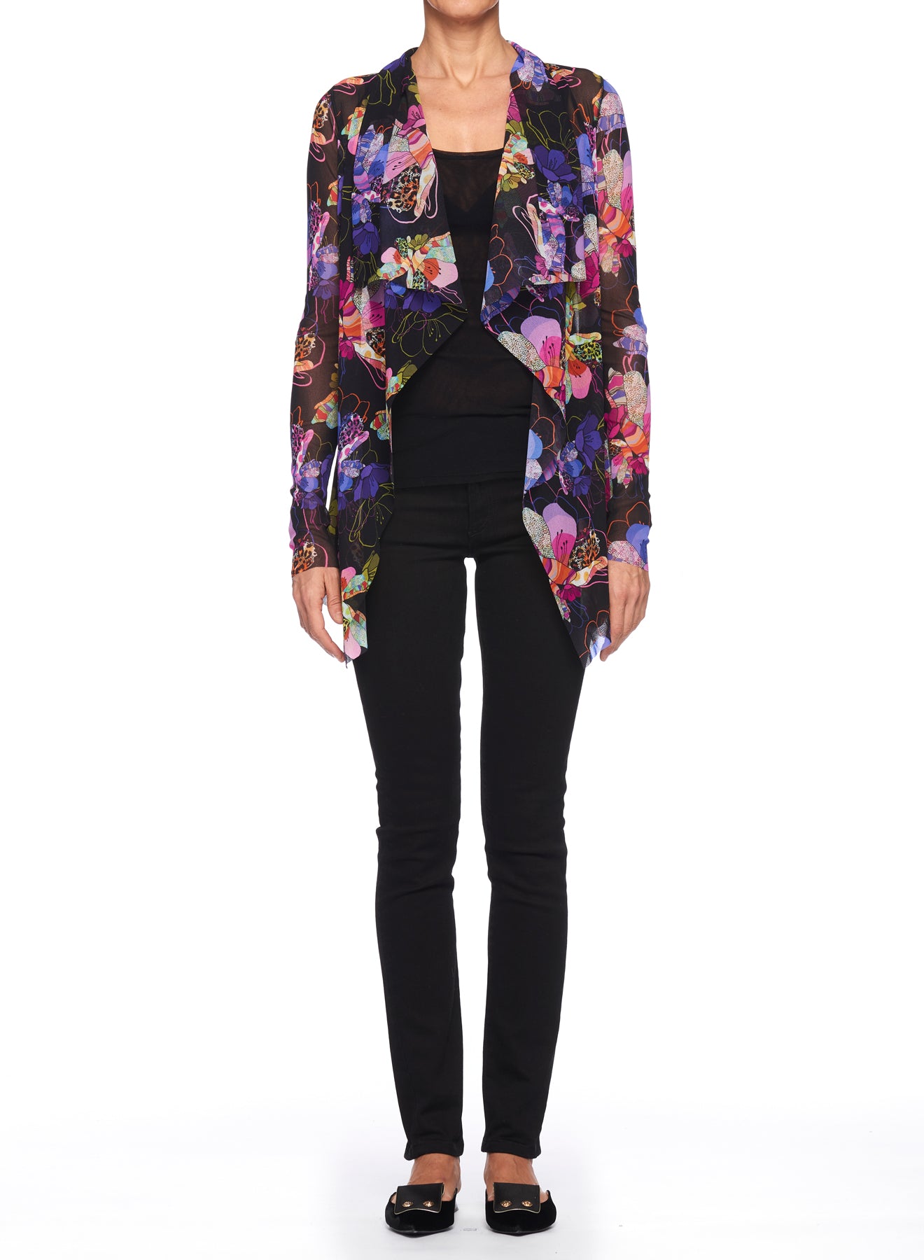 A person wearing the Fuzzi Woman Boho-Chic Floral Mesh Cardigan, a vibrant open-front design with sheer fabric and a floral print, stands against a plain white background over a black top and black pants. The stylish ensemble is completed with sleek black shoes.