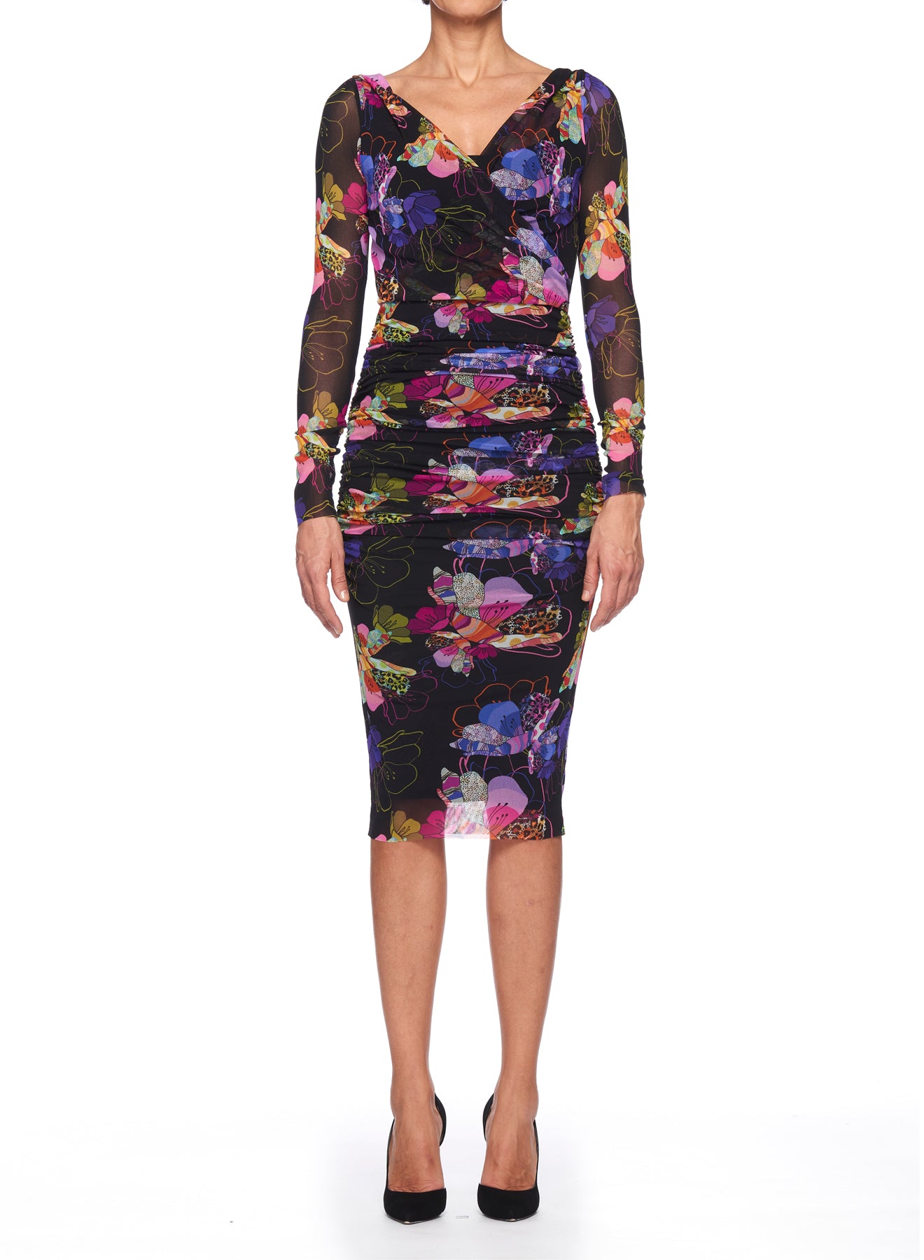 A woman wearing the Fuzzi Woman Mesh Floral Midi Dress, which boasts a vibrant floral print on a fitted black design, stands facing forward against a white background. The dress features long sleeves and a knee-length hem, beautifully showcasing ruched detailing. She completes the look with elegant black high heels.