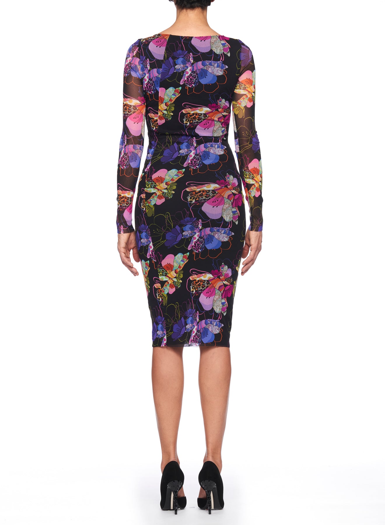 A person is wearing the Fuzzi Woman Floral Midi Dress, characterized by its vintage floral print and sheer mesh fabric on the long sleeves, standing with their back towards us. The knee-length dress is complemented by black high-heeled shoes against a plain white background.