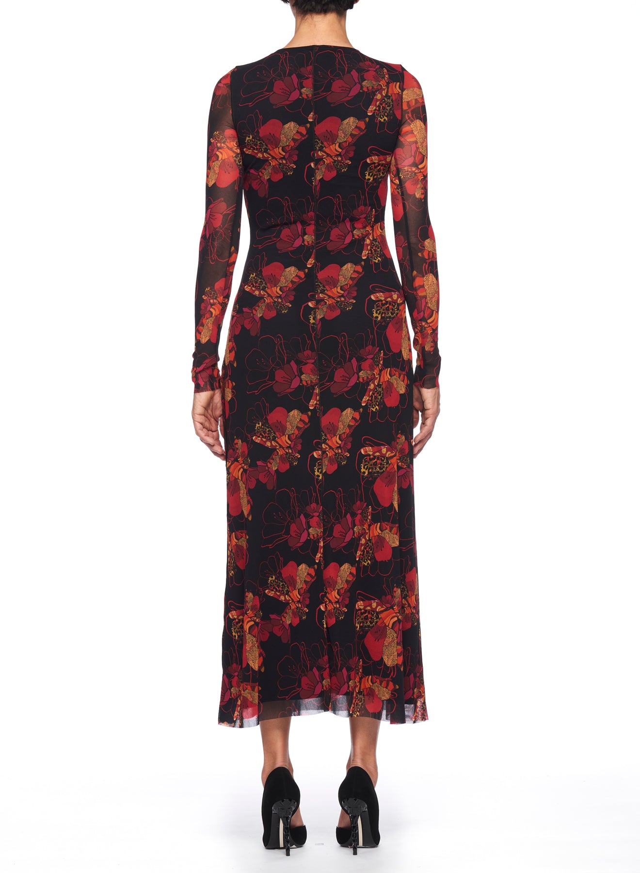 A person is wearing the Fuzzi Woman Romantic Floral Mesh Dress, featuring a vintage style with long sleeves and a floral print in shades of red, orange, and black. The knee-length midi dress pairs well with their black heels as they stand on a white background, facing away from the camera.