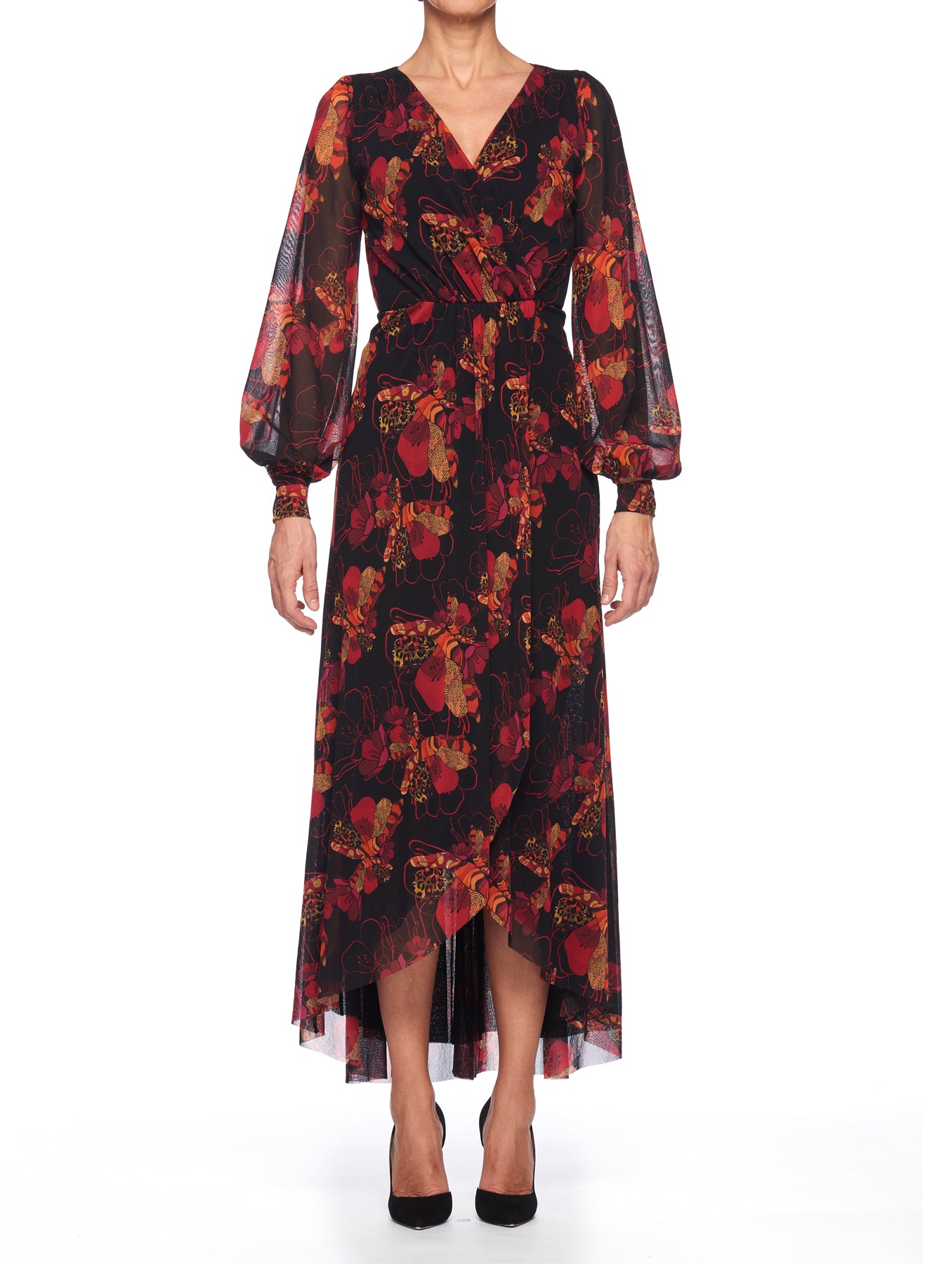 A person models a vintage piece from Fuzzi—a long Dramatic Floral Wrap Dress in black, adorned with red and orange floral patterns. The dress features a V-neck and sheer, long sleeves, embodying an elegant wrap silhouette. They complete the look with black high-heeled shoes against a plain white backdrop.