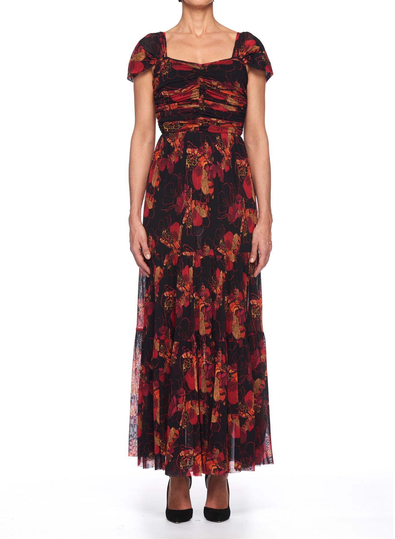 A person is modeling the Fuzzi Woman Floral Maxi Dress, a vintage piece featuring a floral pattern with capped sleeves, a fitted bodice, and a flowing skirt. The dress displays shades of red, orange, and black. They complement the look with black high heels against a crisp white background.