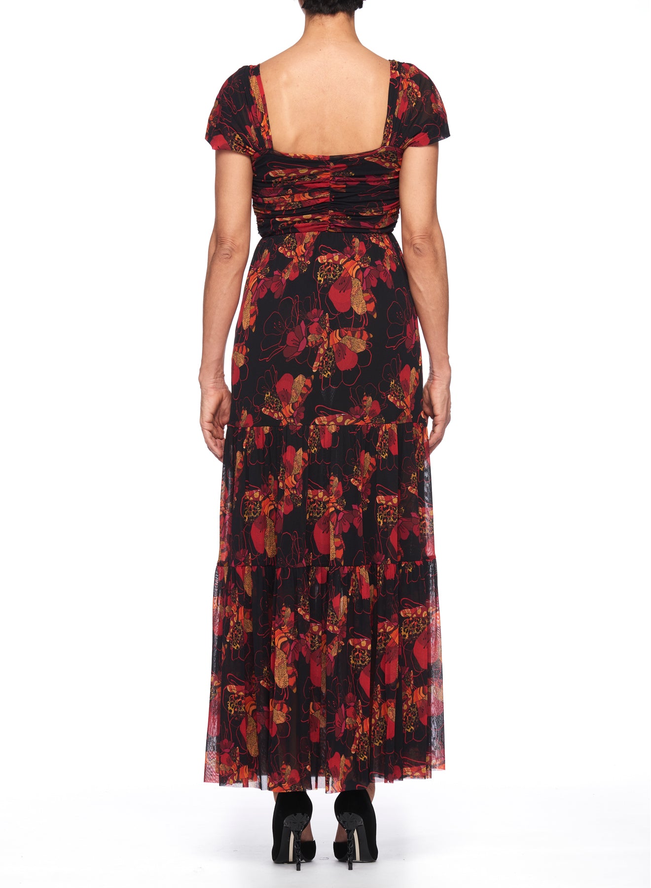 An individual is wearing a vintage piece, the Fuzzi Woman Floral Maxi Dress by Fuzzi, a floor-length black maxi dress embellished with a red floral print. Featuring short sleeves and a square neckline visible from the back, they stand against a plain white background, stylishly paired with black heels.