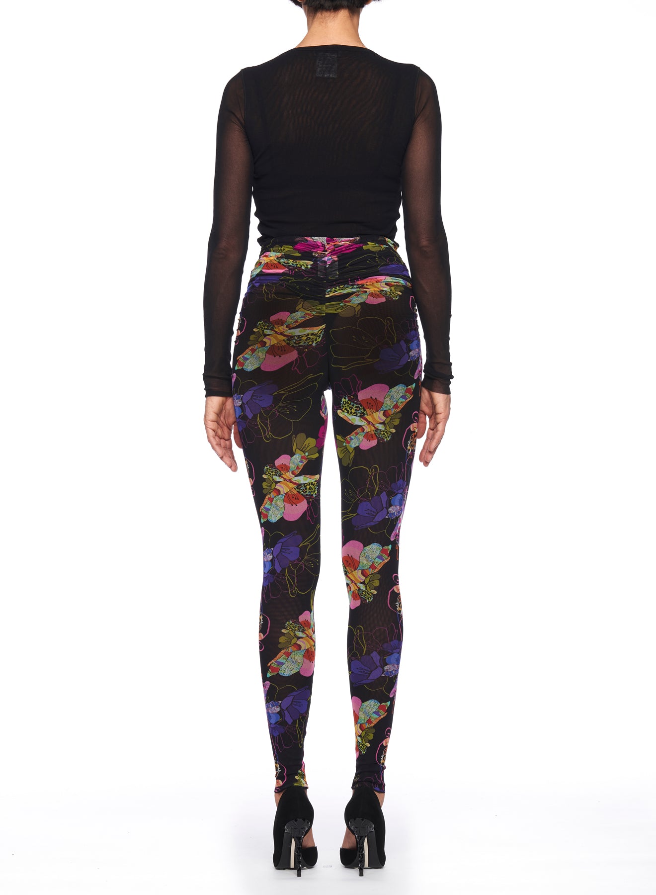 A person stands with their back to the camera, wearing a sheer black long-sleeve top paired with Fuzzi Woman Floral Leggings from Fuzzi. They complete the outfit with black high-heeled shoes against a plain white background.