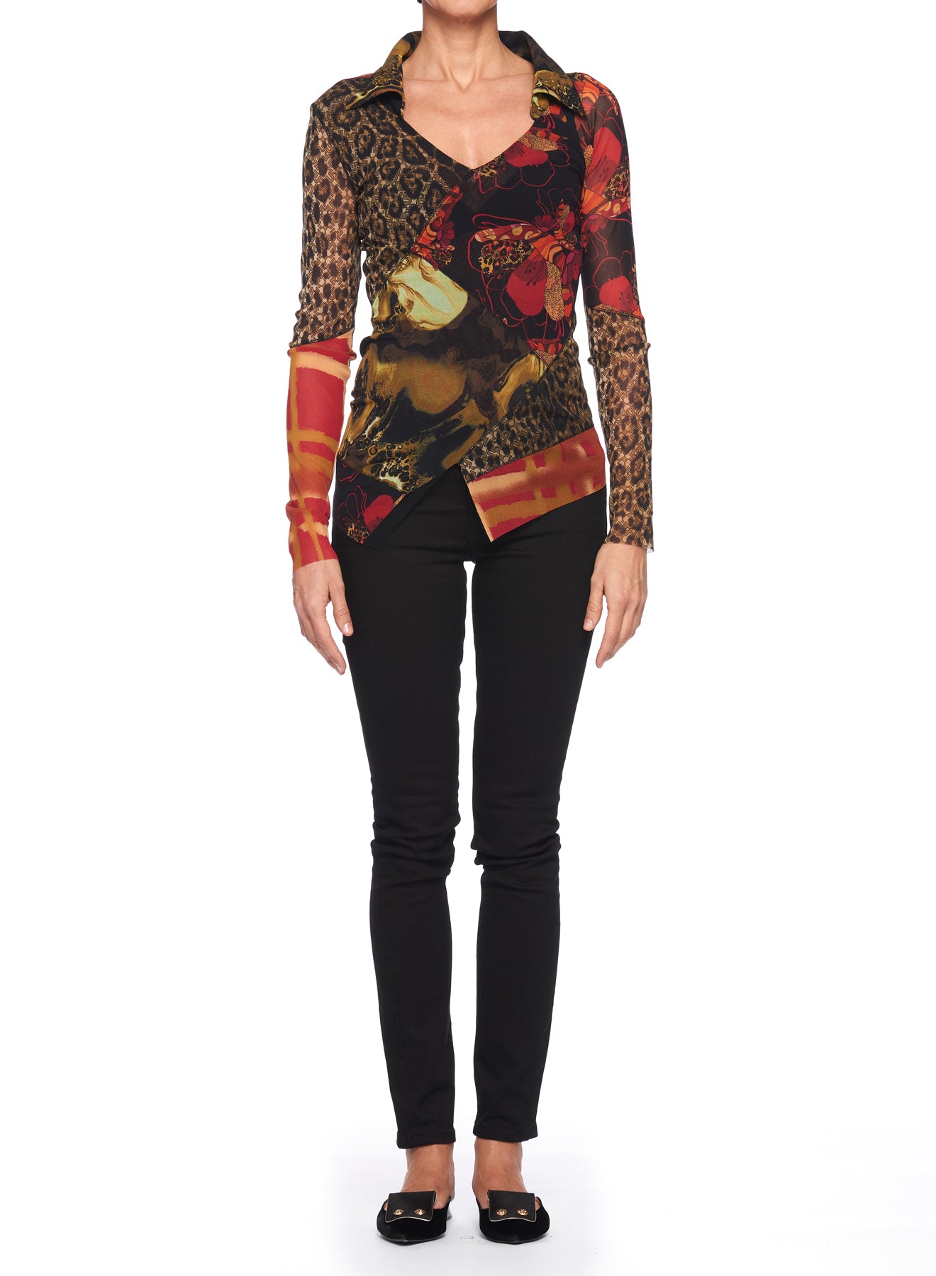 A person is dressed in the Fuzzi Woman Mixed-Print Mesh Top, a long-sleeved blouse featuring a multicolored patchwork design with various patterns, including animal floral prints. They pair it with black pants and black flats while standing against a plain white background, hands by their sides.