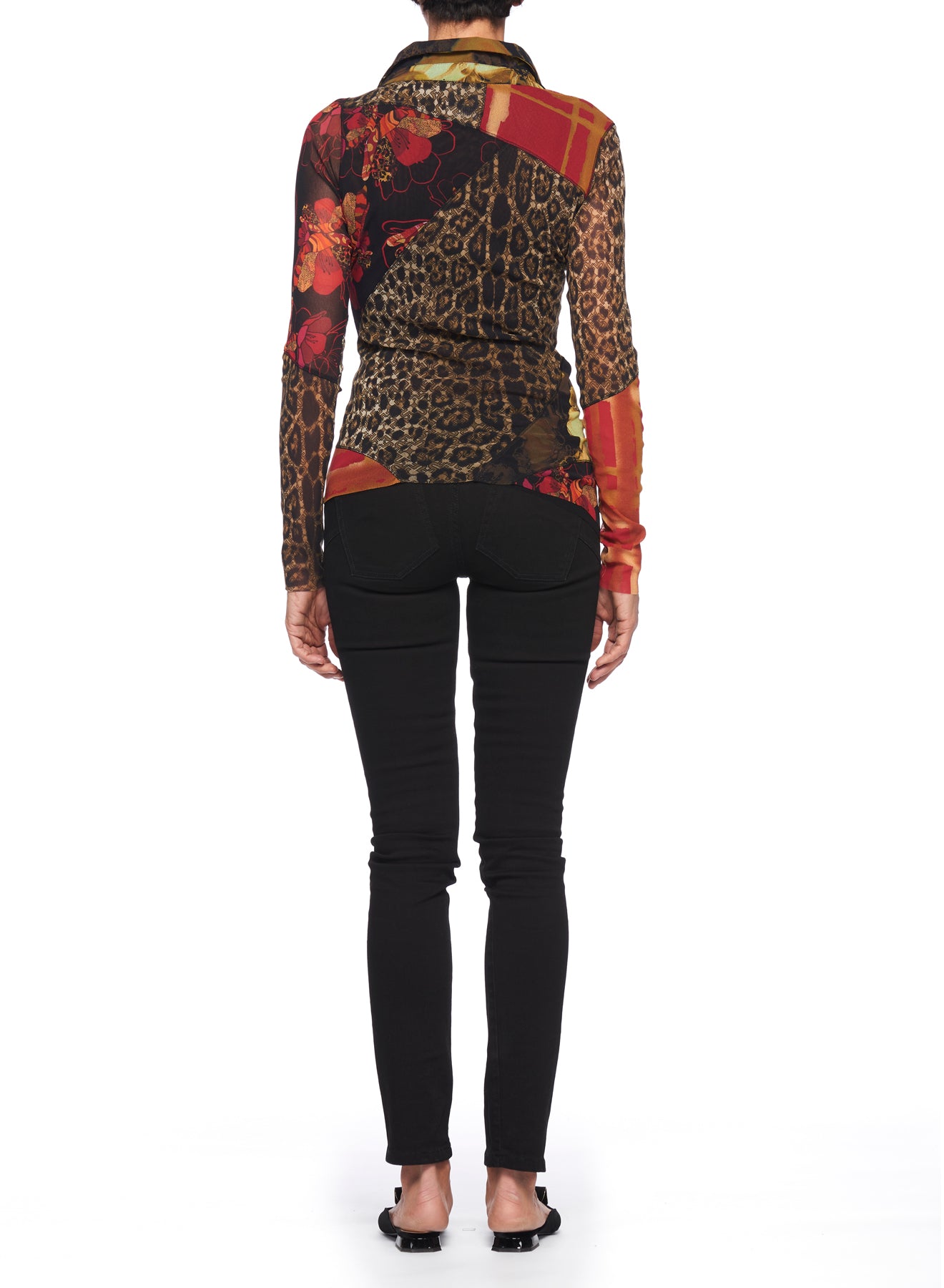 A person facing away, wearing the Fuzzi Woman Mixed-Print Mesh Top—a long-sleeved, asymmetrical shirt with animal floral prints—paired with black jeans and black sandals, stands against a white background.