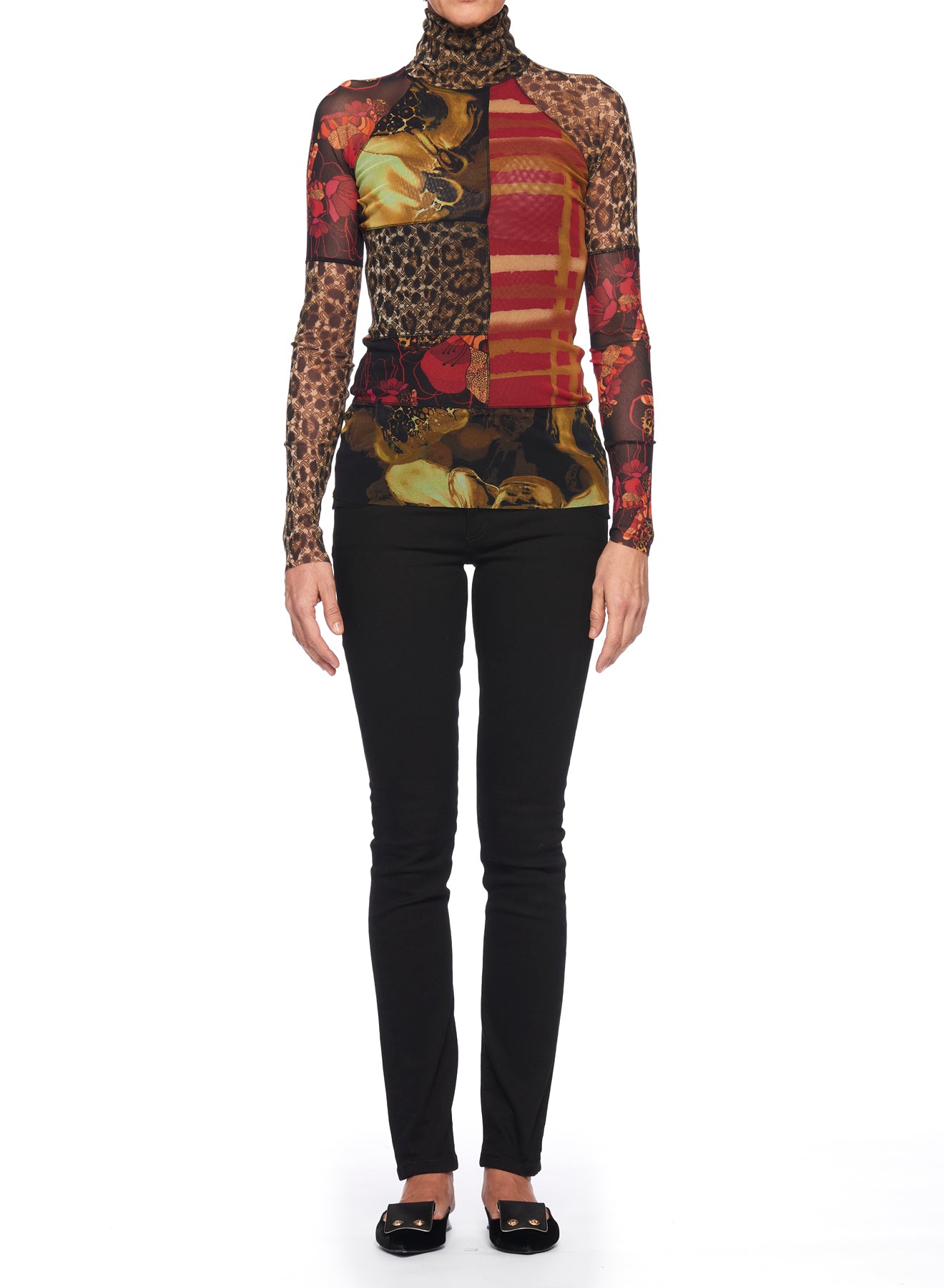 A person stands against a white background wearing the Fuzzi Woman Bold Mixed-Print Mesh Turtleneck, which features red, leopard, and floral prints on sheer mesh fabric, paired with black pants. They complete the ensemble with black shoes.