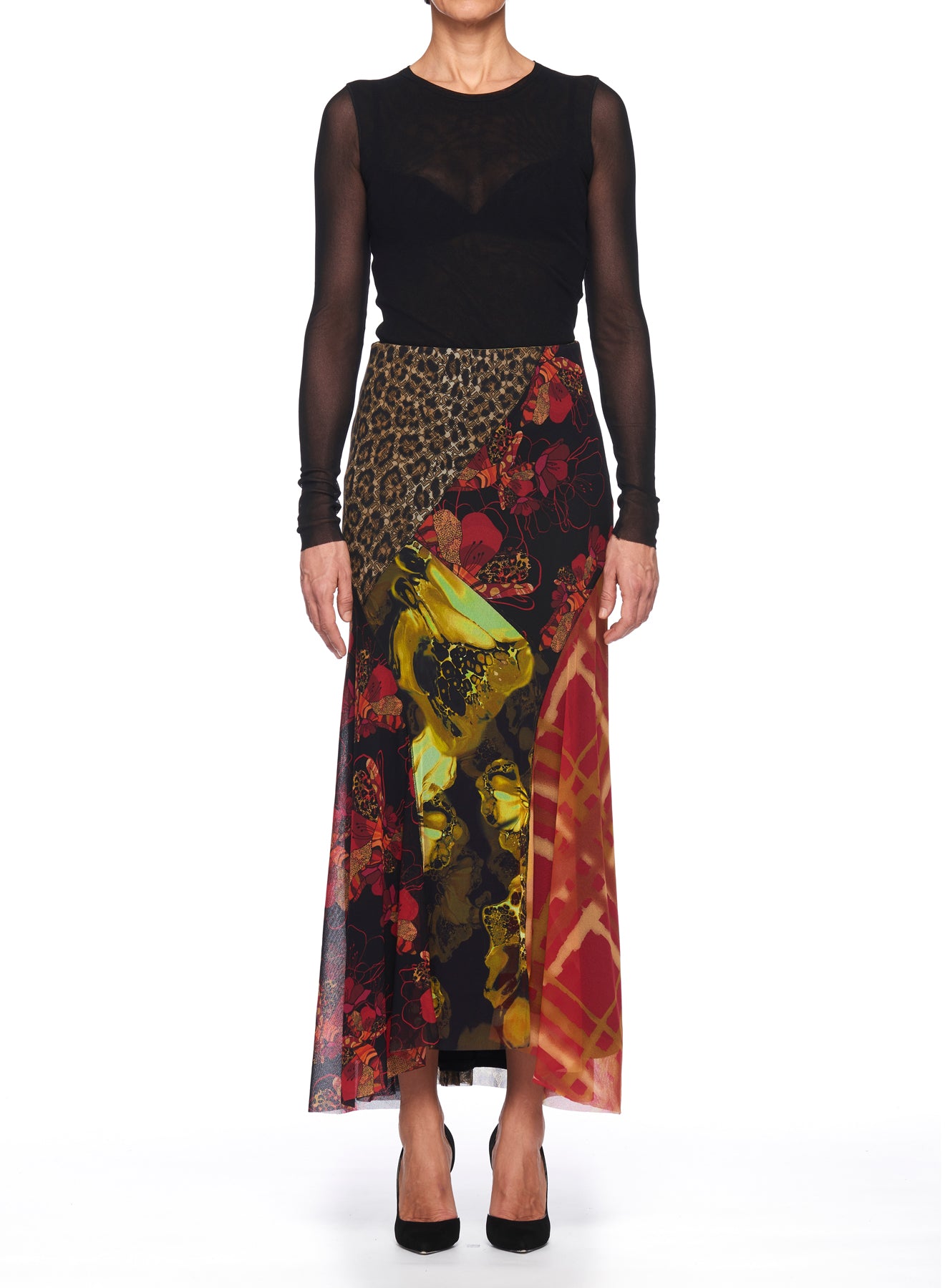 A person showcases the Fuzzi Woman Mixed-Print Mesh Long Skirt, a vintage piece featuring vibrant floral and animal prints. The asymmetrical hemline adds flair, perfectly complementing a sheer, long-sleeve black top. Standing against a white background, they complete the look with stylish black heels from Fuzzi.