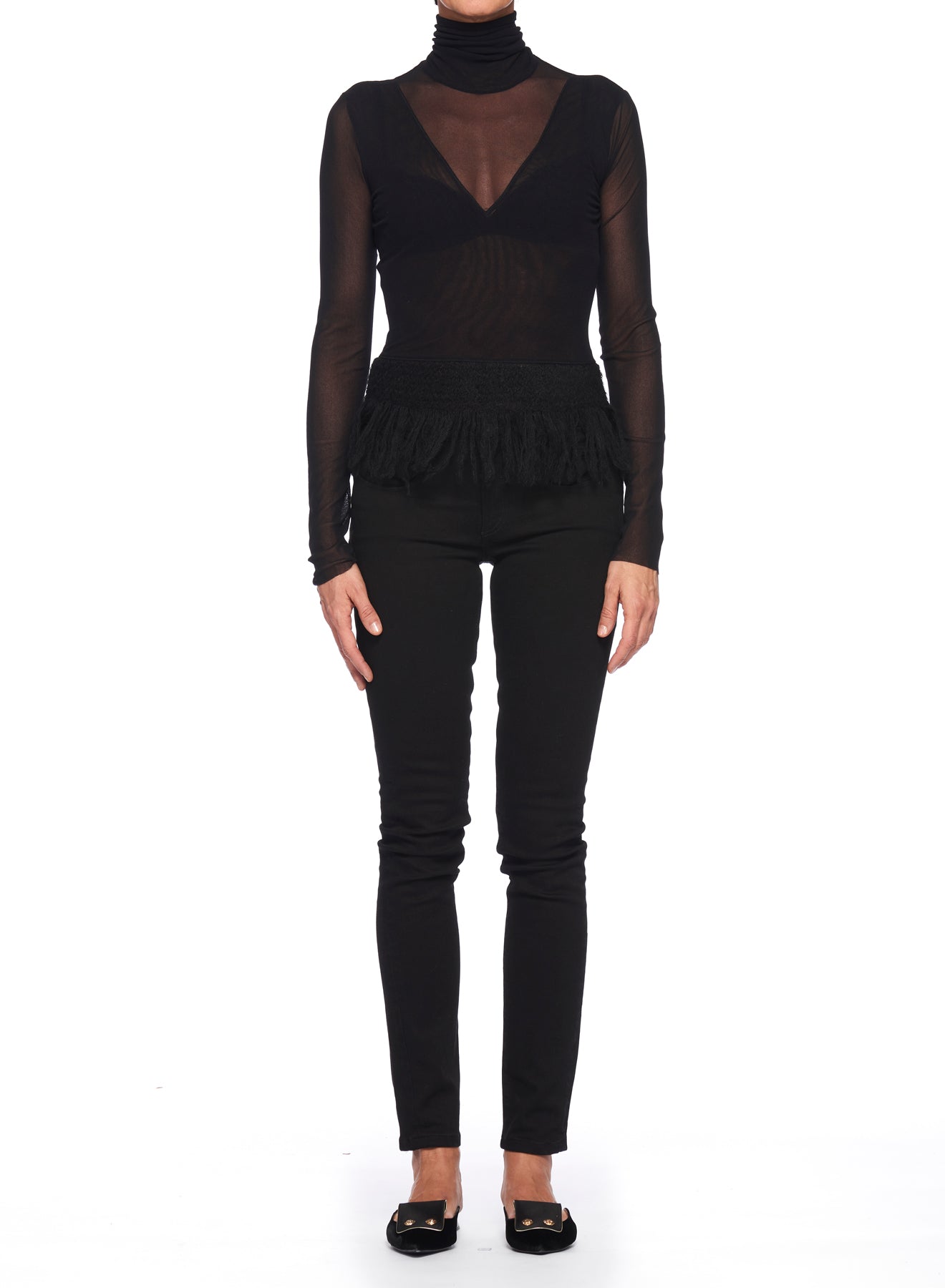 A person is wearing the Fuzzi Woman Black Mesh Top with High Neckline, paired with black fitted pants and flat shoes. The plain white background highlights their minimalist style, as their arms rest calmly at their sides.