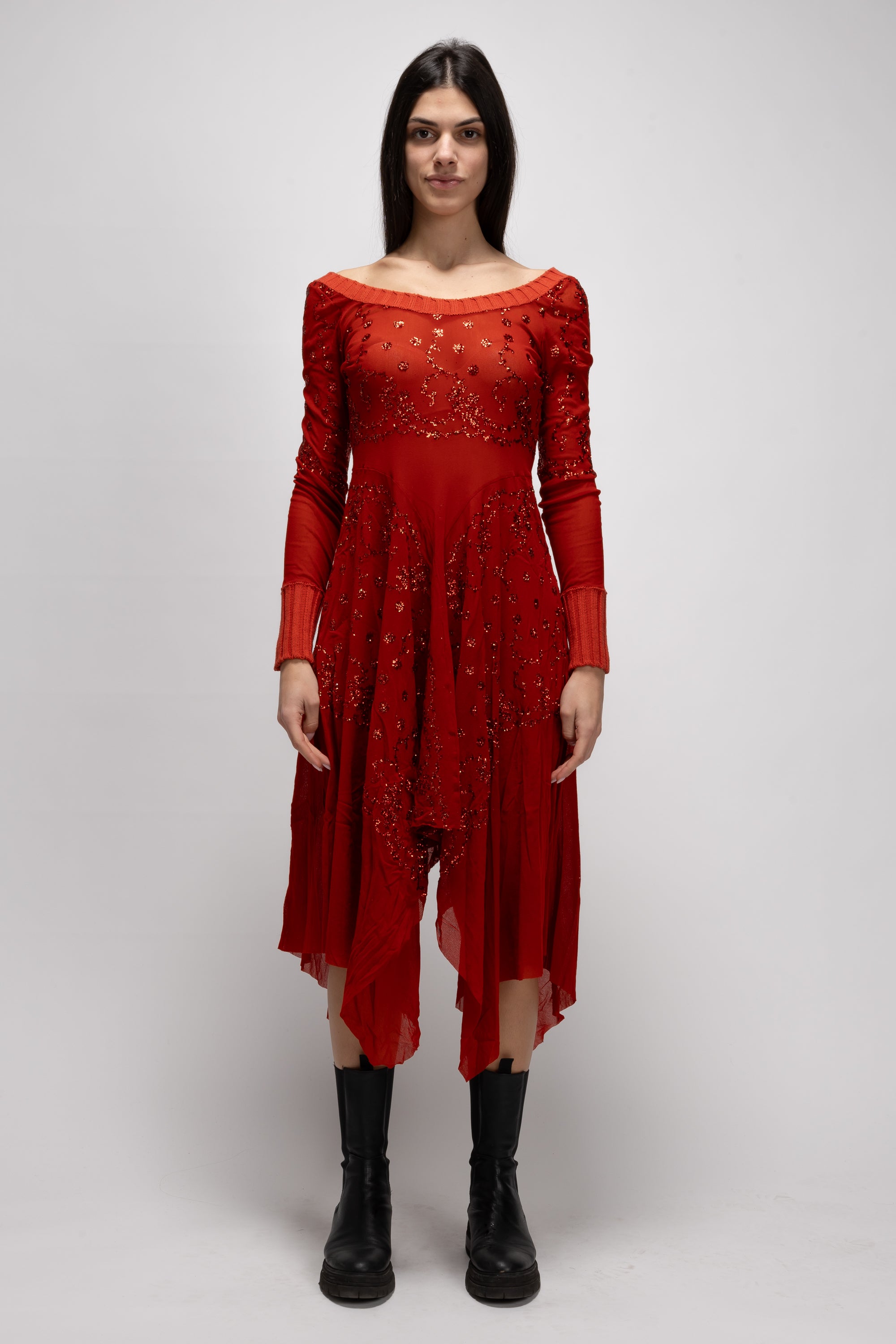 A woman stands confidently against a plain background, wearing the Vintage Woman Red Dress from Jean Paul Gaultier's Spring/Summer 1995 collection, adorned with intricate beading and patterns. Her outfit is complemented by black boots as she gazes directly at the camera.