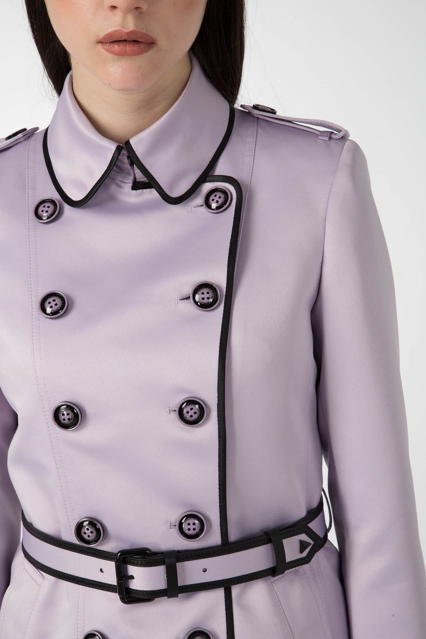 A person wears the Antonio Croce Taylor Trench Coat with Belt, featuring a vintage double-breasted design in light purple with black trim and buttons. The plain white background enhances this classic Antonio Croce piece.